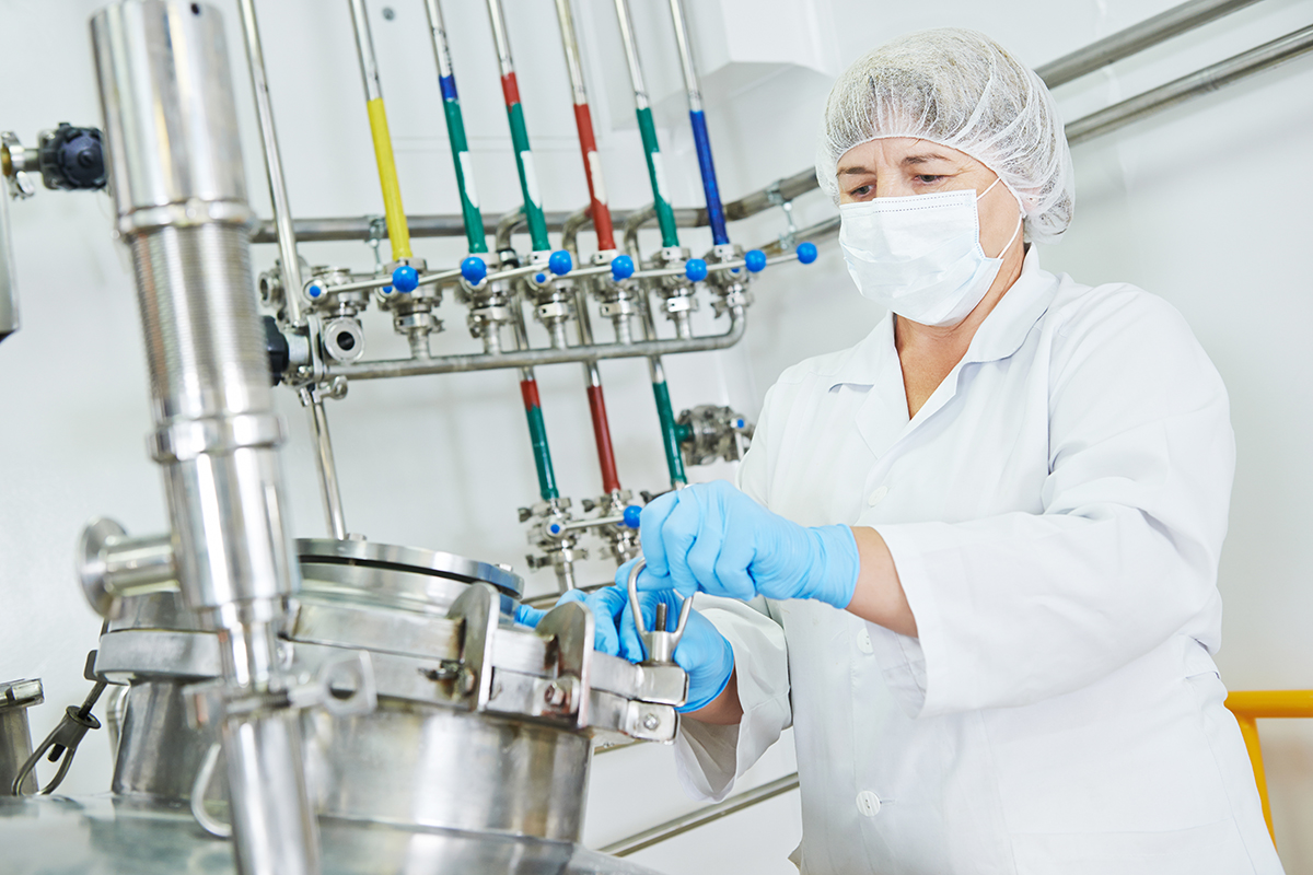 pharmaceutical worker with equipment mixing tank on production line in pharmacy industry manufacture factory