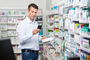 Mid adult male consumer checking information on mobile phone while holding product in pharmacy