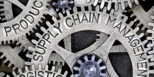 Macro photo of tooth wheel mechanism with SUPPLY CHAIN MANAGEMENT, PRODUCT, LOGISTICS, SYSTEM, PROFIT, PLAN and NETWORK words imprinted on metal surface
